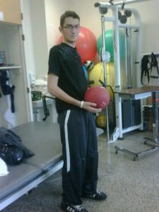 Image of Nicholas Morihovits at rehab bouncing the ball and standing on his own